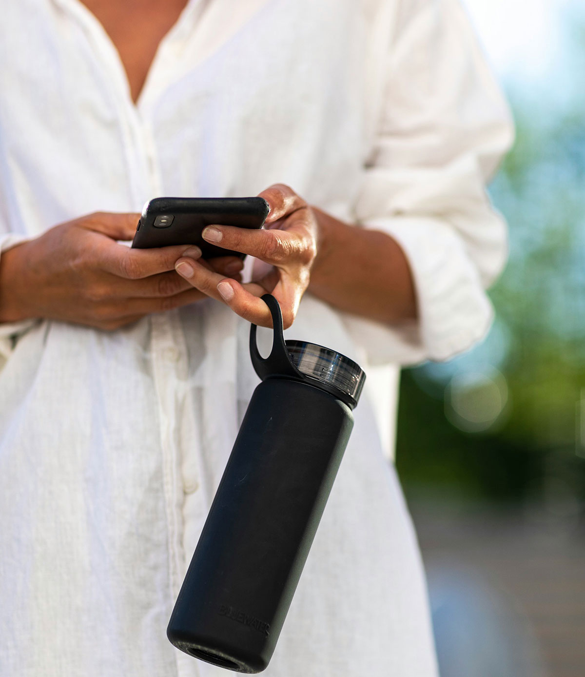 woman holding a refillable drink bottle checking her phone